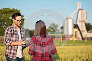 Two happy young female and male farmers or agronomists talking in a wheat field, consulting and discussing photo