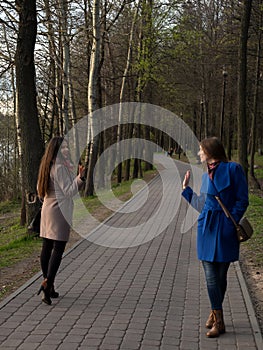 Two happy young girls met each other in the park. Female friendship. Walk in the park outdoors