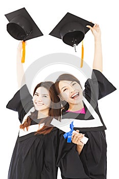 Two happy young graduate students holding hats and diploma