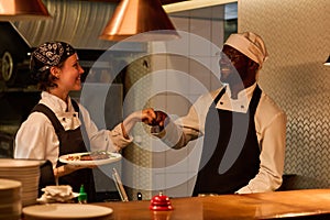 Two happy young intercultural kitchen workers giving each other punch bump