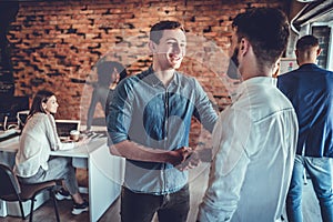 Two happy young men shaking hands while standing in the office