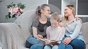 Two happy young mother reading book with teenage daughter having positive emotion