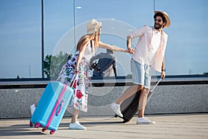 Two happy young tourists holding hands and running in front of an airport terminal.