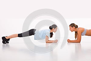 Two happy young woman doing push-ups in gym