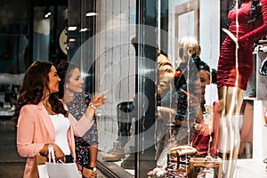 Two happy young women with shopping bags having fun and pointing finger in the shop window