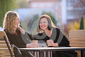 Two happy young women sitting at city street cafe havinh fun time together during coffee break photo