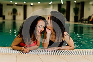 Two happy young women in swimwear standing together, having fun at the swimming pool