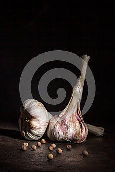 Two heads of garlic and black pepper on a dark background