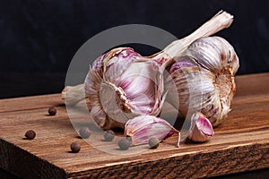 Two heads of garlic and black pepper peas on a wooden board