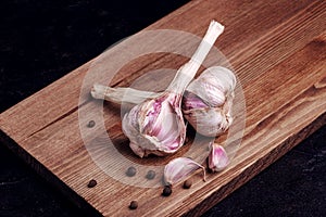 Two heads of garlic and black pepper peas on a wooden board