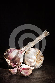 Two heads of garlic and cloves lying on a dark background