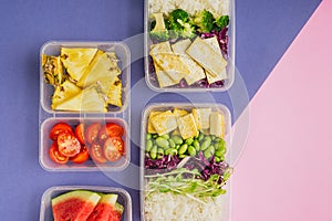 Two healthy asian-style plant-based lunch boxes knolled together on blue and pink background