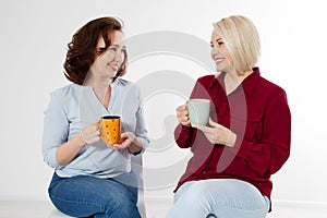 Two healthy and beautiful middle aged women drinking tea and talking isolated on white background. Woman support woman. Happy