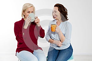 Two healthy and beautiful middle aged women drinking tea and talking isolated on white background. Woman support woman. Happy