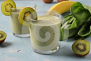 Two healthy detox smoothie kiwi, banana, spinach in glasses on light blue background with fresh ingredients. Diet and weight loss