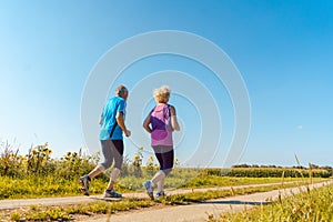 Two healthy senior people jogging on a country road in summer