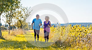 Two healthy senior people jogging on a country road in summer photo