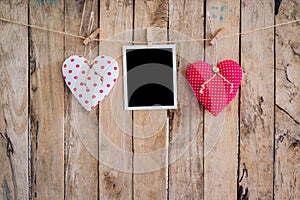 Two heart and photo frame hanging on clothesline rope with wooden background.