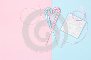 Two heart shaped candy canes with gift box on pastel blue and pink background. Sweet love, marriage proposal minimal concept