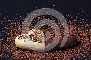 Two heart-shaped chocolates made of milk and white chocolate on the slate board, covered in grated chocolate