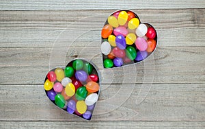 Two heart shaped cookie cutters with jelly beans on wood background