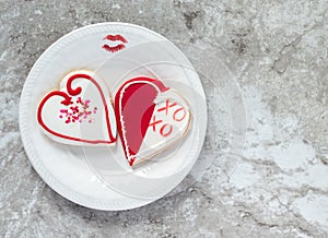 Two heart shaped cookies with a lipstick kiss and a plate on a gray marble counter