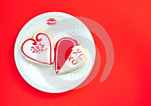 Two heart shaped cookies with a lipstick kiss and a plate on a red background