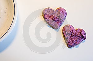 Two heart shaped cookies spread with blueberry curd raw cream for Valentine\'s Day on white table surface top view