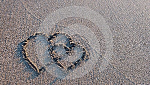 Two hearts drawn on brown sand of paradise beach