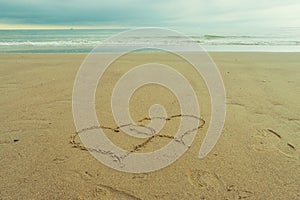 Two hearts drawn in the sand of a beach with a quiet sea and incoming clouds in the back