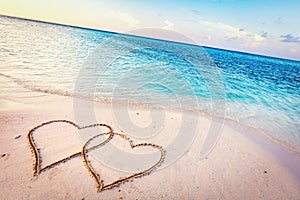 Two hearts drawn on sand of a tropical beach at sunset.