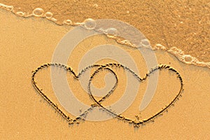 Two hearts drawn in the sea sand with the soft wave. Love.