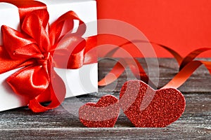 Two hearts with gift box on a wooden background. Couple of different red hearts. Valentine`s day card.
