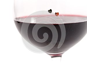 Two hearts on a glass with red wine on white background