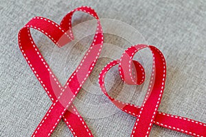 Two hearts made from red ribbon on linen textile