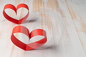 Two hearts made of ribbon on wooden background.