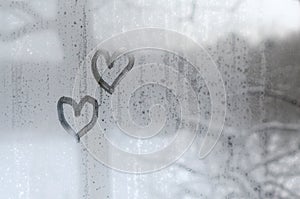 Two hearts painted on a misted glass in winter