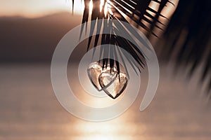 Two hearts on palm tree, background of romantic sea sunset. Couple in love. Christmas holiday, Valentine`s Day concept