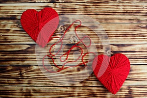 Two hearts of red color tied by a thread lie on a wooden background