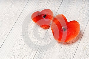 Two hearts from red flower petals in heart shape over white wood