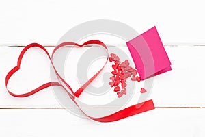 Two hearts of red ribbon with a few small hearts and greeting card on white wooden background.