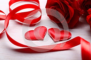 Two hearts, ribbon and red roses on table