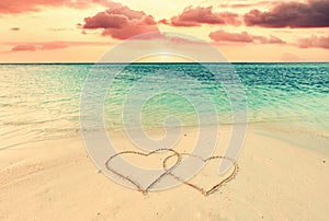 Two hearts on sand on tropical beach at sunset