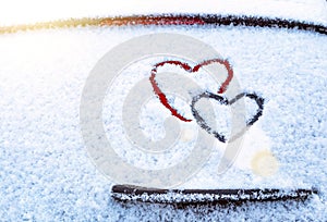 Two hearts symbol of love hand drawing painted on snow on the glass above windshield wiper of car. Valentines day, love.