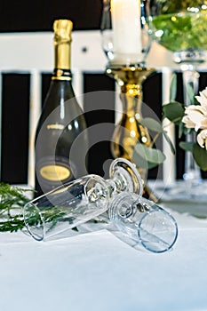 Two high champagne glasses lay on table in front of bottle of champagne