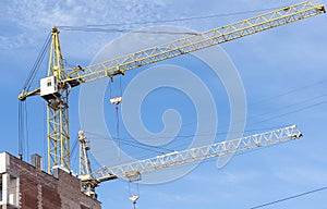 Two high-rise construction cranes and unfinished monolithic building on the blue sky background. Building construction