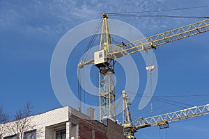 Two high-rise construction cranes and unfinished monolithic building on the blue sky background. The construction of