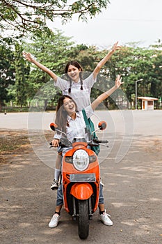 Two high school girls riding motorbikes standing while celebrating graduation