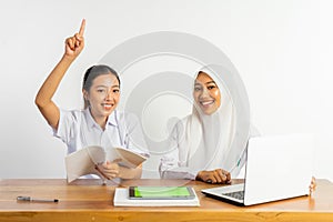 two high school girls sitting at desk while pointing finger