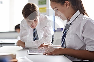Two High School Students Wearing Uniform Working Together At Desk Using Digital Tablet
